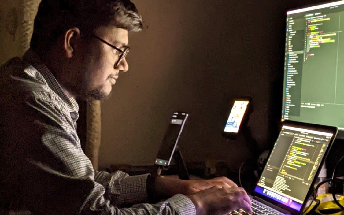 Muhammad Sheraz coding at his desk in Islamabad, with test phones and an external monitor